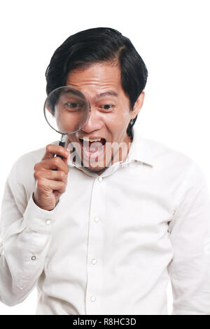 Photo image portrait of a funny young Asian businessman looked very happy, surprised and smiling to find something while looking into magnifying glass Stock Photo