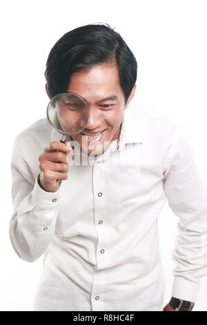 Photo image portrait of a funny young Asian businessman looked very happy and smiling to find something while looking into magnifying glass, close up  Stock Photo