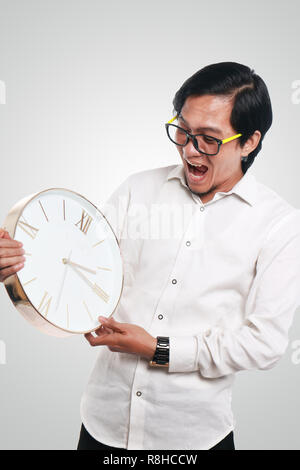 Photo image portrait of a funny young Asian businessman looked shocked while looking a clock that he hold, close up portrait, time or deadline concept Stock Photo