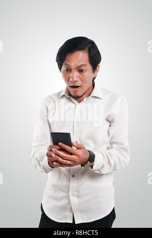 Photo image portrait of a funny young Asian man shocked while looking his smart phone. Holding phone with both hands while reading message on it Stock Photo