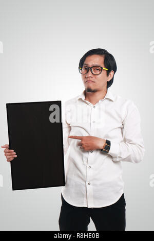 Photo image portrait of funny Asian businessman or teacher or student showing empty blackboard with sad face, holding blackboard with one hand while o Stock Photo