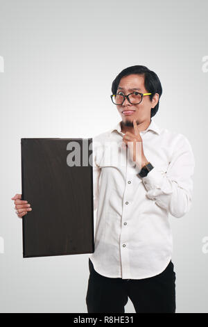 Photo image portrait of crazy Asian businessman or teacher or student holding blackboard with funny confused face and thinking gesture Stock Photo