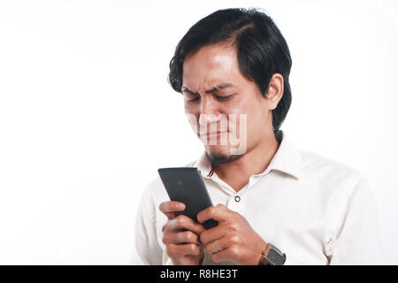 Photo image portrait of a funny young Asian man seriously texting on his smart phone. Holding phone with both hands while reading message on it, over  Stock Photo