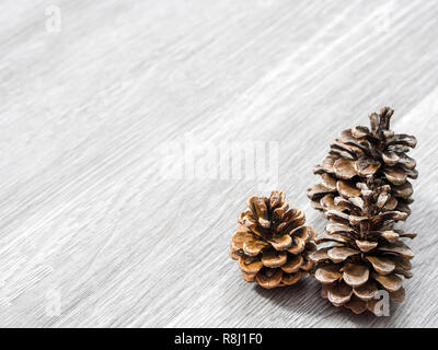 Three brown pine cones laying in the corner of image and isolated on a background of gray wood grain texture flooring making a beautiful winter or Chr Stock Photo