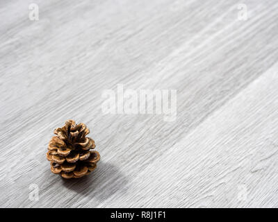 A brown pine cone laying in the corner of image and isolated on a background of gray wood grain texture flooring making a beautiful winter or Christma Stock Photo