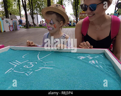 Little girl painting on green sand with her mother Stock Photo