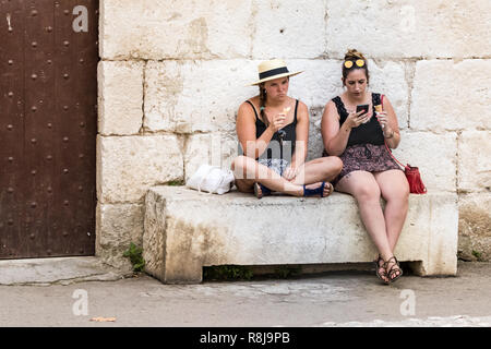 Croatia, Split - September 22th, 2018: Two young women sitting outdoors eating ice cream and using a mobile in the old city of Split, Croatia. Stock Photo