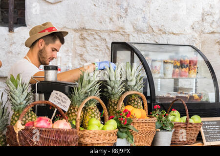 Croatia, Split - September 22th, 2018: A young man wearing a hat and blue gloves squeezing fruits to make fresh juice in a street market in Split, Cro Stock Photo