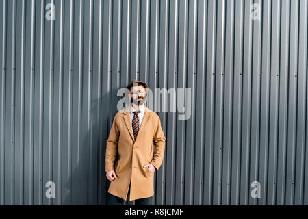 handsome businessman in coat standing against sunshine near textured wall Stock Photo