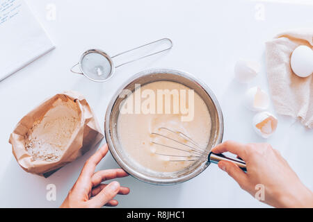 Woman's hands whipping eggs and flour in bowl. Flat lay composition process making batter. Stock Photo