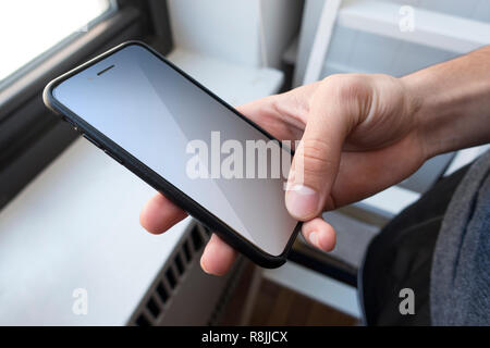 Hand holding and using  a cell phone young man inside near window Stock Photo