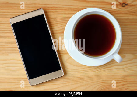 Top view of gold smartphone with a cup of hot tea on wooden table Stock Photo