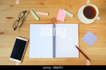 Working desk with white opened notebook, pen, smartphone, eyeglasses, memo paper and a cup of hot tea on wooden desk Stock Photo