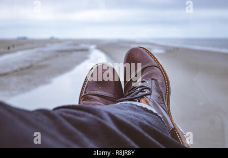 Closeup of leather boots under wool blankets with a stunning view at a northern sea beach.