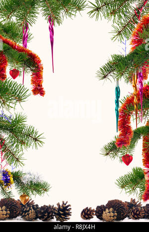 Christmas tree branches decorated with colorful ornaments and pine cones framed on off-white background with copyspace in the center Stock Photo