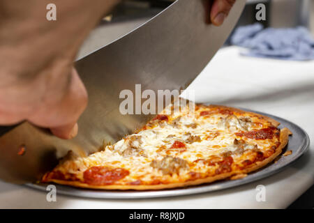 Chef cutting a pizza with a mezzaluna in a restaurant.  Close up side view.  Hands only visible. Stock Photo