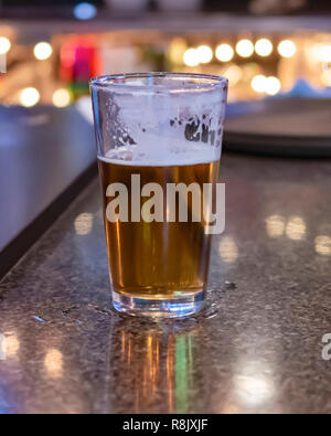 A half drunk glass of beer on the bar.  Blurred background.  Bokkeh lights.
