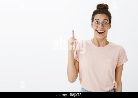 Waist-up shot of happy smart and creative nerdy woman with hairbun in round glasses smiling broadly from excitement and joy as raising index finger in eureka gesture and adding idea or plan Stock Photo