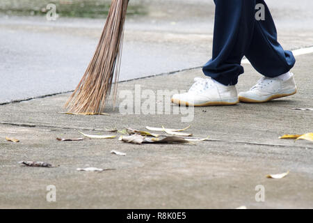 Student sweeping dried leafs on the floor in school. Stock Photo