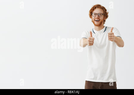 Indoor shot of happy smart and creative good-looking friendly redhead man with beard and moustache pulling hands towards camera in thumbs up gesture liking cheering and supporting Stock Photo