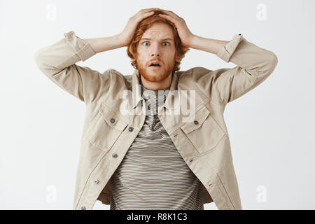 Waist-up shot of worried insecure cute redhead adult husband with beard holding hands on head forgetting buy milk in shop standing nervously, being forgetful and upset over gray background Stock Photo