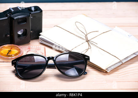 Sunglasses, compass, old film camera and a bunch of letters on a light wooden background. Concept of summer travel destination. Stock Photo