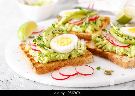 Toasts with avocado guacamole, fresh radish, boiled egg, chia and pumpkin seeds. Diet breakfast. Delicious and healthy plant-based food. Closeup Stock Photo