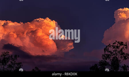 Orange glow of massive thunderstorm clouds approaching at sunset in a landscape panoramic view Stock Photo