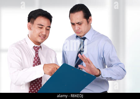 Photo image, portrait of two Asian businessman doing business conversation, staff showing notes while boss showing rejection gesture Stock Photo