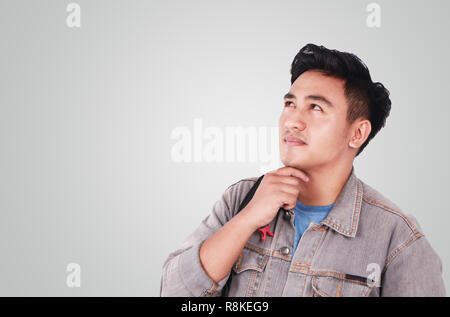Photo image portrait of a cute young Asian male student standing, looking up and thinking Stock Photo