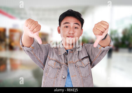 Photo image portrait of a cute young Asian man doing mocking gesture and showing two thumbs down Stock Photo