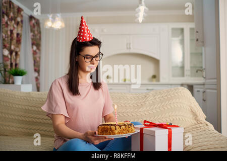 An unhappy girl wearing a hat on her birthday with a cake with c Stock Photo