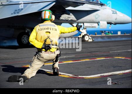 A catapult officer in a yellow shirt known as a shooter, signals the launch of a F/A-18 Super Hornet fighter aboard the Nimitz-class aircraft carrier USS Harry S. Truman December 7, 2018 in the Atlantic Ocean. Yellow shirts are worn by aircraft handlers, aircraft directors, Catapult Officers and Arresting Gear Officers considered the most difficult and important job on the flight deck. Stock Photo