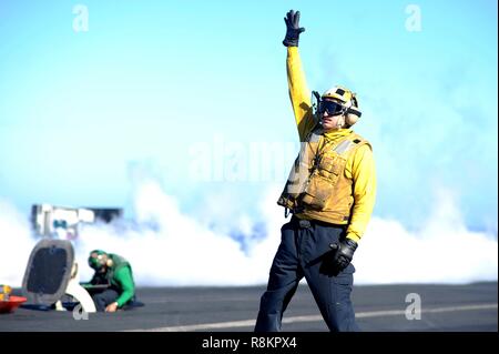An Aircraft Handler in a yellow shirt, signals the launch of a F/A-18 Super Hornet fighter aboard the Nimitz-class aircraft carrier USS Harry S. Truman December 7, 2018 in the Atlantic Ocean. Yellow shirts are worn by aircraft handlers, aircraft directors, Catapult Officers and Arresting Gear Officers considered the most difficult and important job on the flight deck. Stock Photo