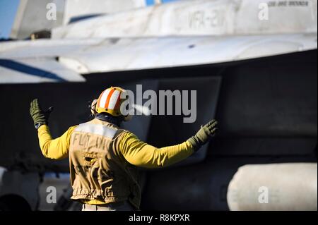 A Flight Director in a yellow shirt, signals a F/A-18 Super Hornet fighter aboard the Nimitz-class aircraft carrier USS Harry S. Truman December 7, 2018 in the Atlantic Ocean. Yellow shirts are worn by aircraft handlers, aircraft directors, Catapult Officers and Arresting Gear Officers considered the most difficult and important job on the flight deck. Stock Photo