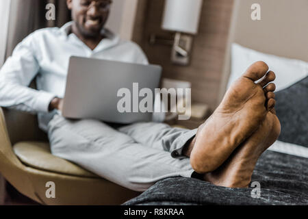 selective focus of barefoot african american man using laptop in hotel room Stock Photo