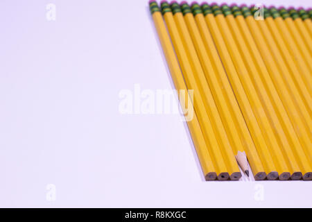 Dull pencils in a row with one sharpened pencil on a white table with copy space Stock Photo