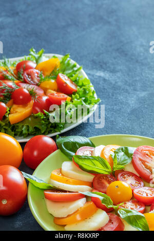 Two plates with salad of tomatoes with herbs on dark grey background with copy space. Stock Photo