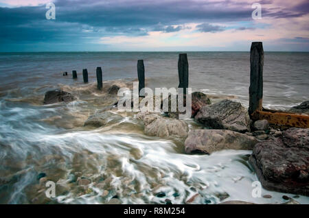 Water flowing over the remains of groynes along the pebbled beach at Llanddulas, North Wales. Stock Photo