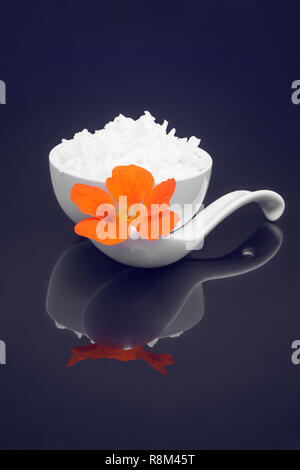 White rice in white dish garnished with edible orange Nasturtium flower on black background Stock Photo