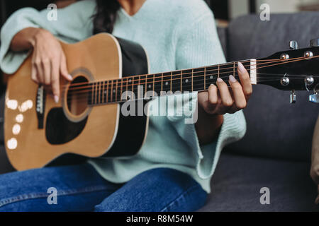 cropped image of mixed race girl in turquoise sweater playing acoustic guitar on sofa at home Stock Photo