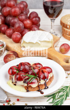 Bruschetta of Camembert or brie cheese with red grapes, rosemary and balsamic. crostini. Gourmet wine snacks for foodies. Italian antipasti. Selective Stock Photo