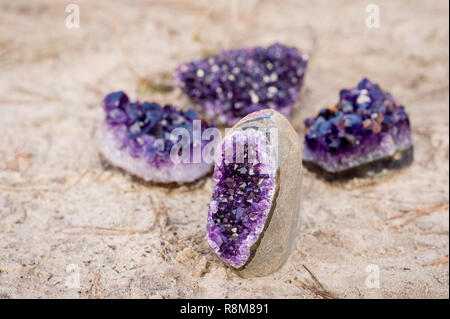 4 small amethyst gemstones with the focus on the front one, laying on the beach Stock Photo