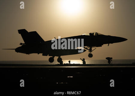 A U.S. Navy F/A-18E Super Hornet fighter aircraft takes off from the flight deck of the Nimitz-class aircraft carrier USS John C. Stennis silhouetted by the setting sun December 11, 2018 in the Arabian Sea. Stock Photo