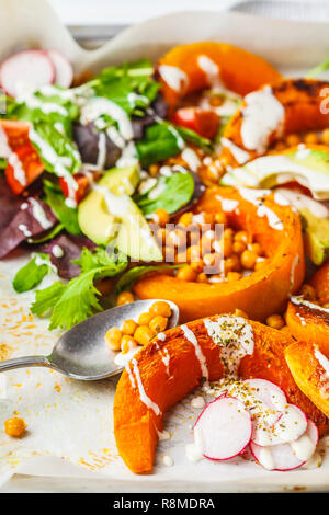 Baked pumpkin with chickpeas on a baking sheet with avocado, tahini and vegetables. Stock Photo