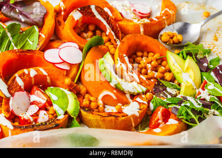 Baked pumpkin with chickpeas on a baking sheet with avocado, tahini and vegetables. Stock Photo