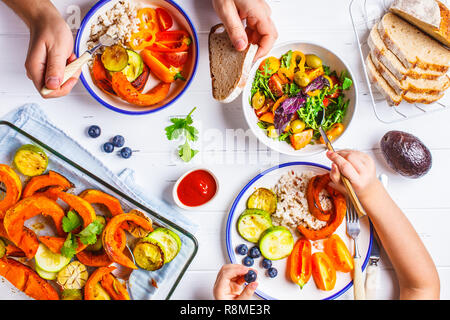Flat lay of family hands eating healthy food. Vegan lunch table top view. Baked vegetables, fresh salad, berries, bread on a white background. Stock Photo