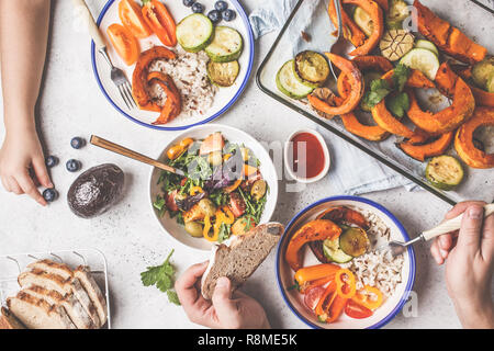 Flat lay of family hands eating healthy food. Vegan lunch table top view. Baked vegetables, fresh salad, berries, bread on a white background. Stock Photo