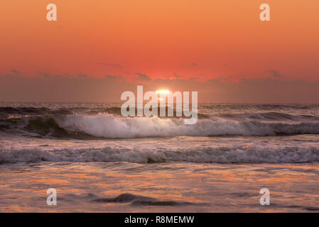 Sunrise beach shot with sun rays shining on waves Stock Photo
