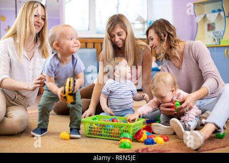 Three woman friends with kids toddlers having a fun sitting on the floor in playroom Stock Photo